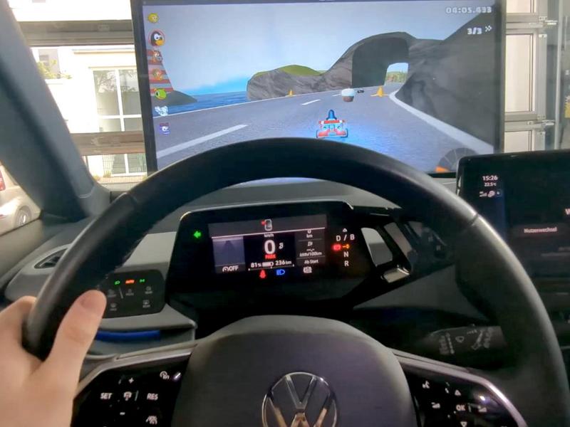 A picture showing in the foreground the steering wheel and dashboard of a Volkswagen ID.3 with Tux driving in SuperTuxKart's Nessie's Pond visible on a screen in front of the car